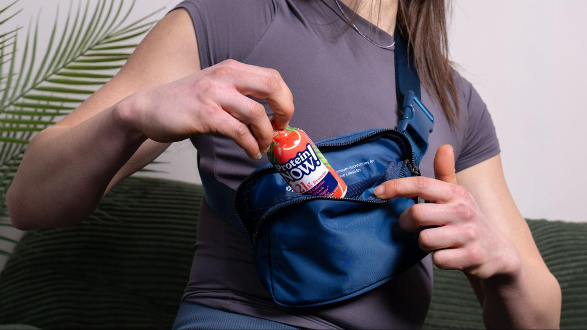 Woman placing a small snack or drink bottle into a blue crossbody bag while seated indoors.