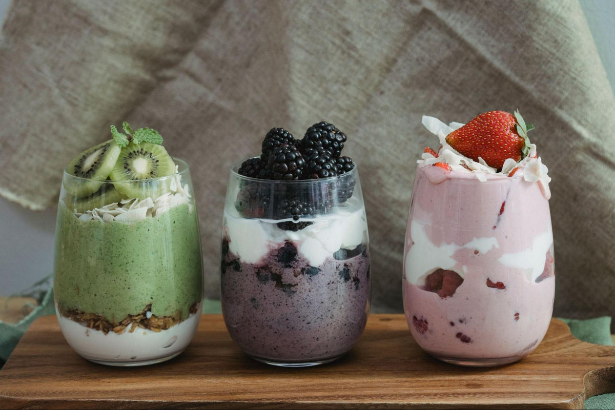 Three fruit smoothies: kiwi, blackberry, and strawberry, topped with their respective fruits, are on a wood cutting board.